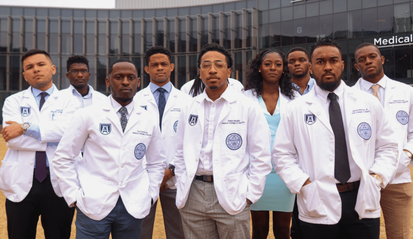 Multiple black male (and one female) medical students look sternly at the camera in white coats.