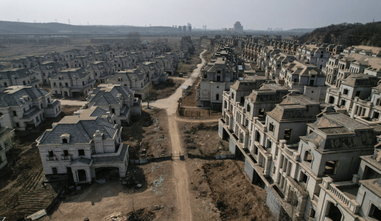 Aerial view of GettyImages-1543006498.jpg showing rows of abandoned, unfinished luxury mansions divided by a dirt road in a dusty, ghost-town development.