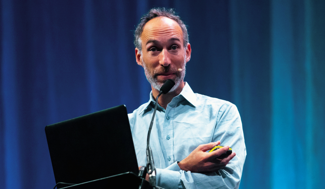 A man holds a laptop on stage while giving a presentation. 