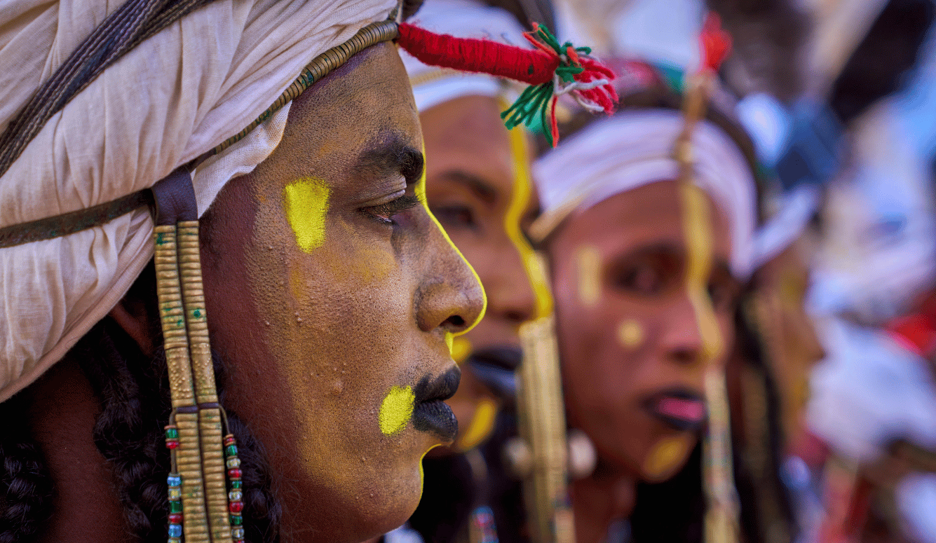 Close-up of Wodaabe men wearing white turbans, beaded ornaments and yellow face paint during a festival in Niger.
