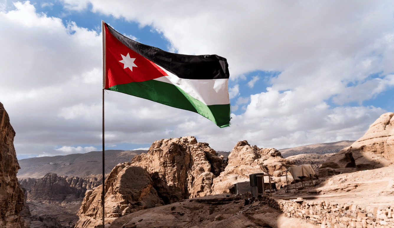 The flag of Jordan blowing in the wind in Petra, Jordan. Three-color flag of Jordan on the background of rocks and mountains in the Jordan desert