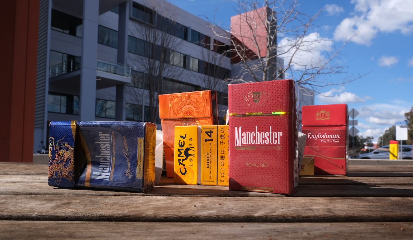 A lost shot of packets of illicit cigarettes arranged on the ground outside.