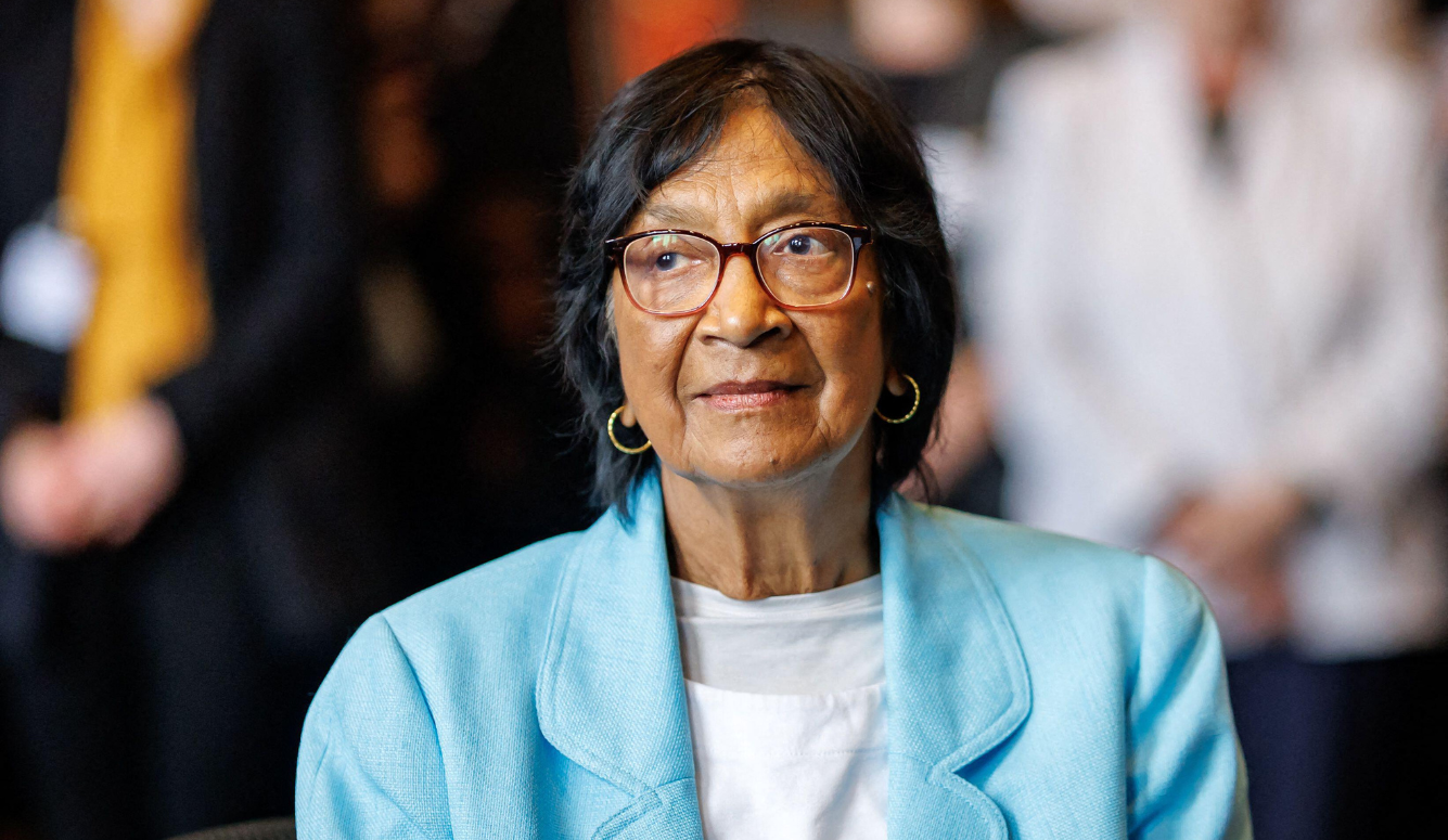 85 year old indian woman Navanethem Pillay, wearing glasses, gold hoop earrings and a turquoise blazer, sits at the Nuremberg Forum.