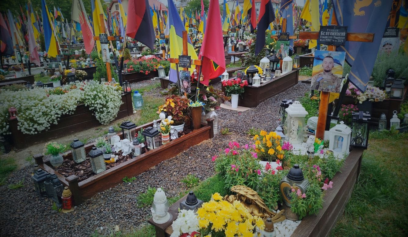 Many colourful graves with plants and colourful flowers on them, as well as flags and photos of the fallen