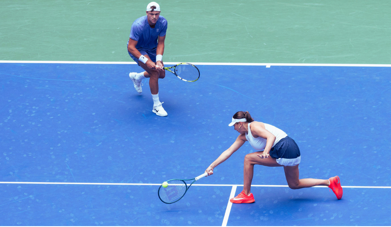 Amanda Anisimova lunges for the ball in mixed doubles with Holger Rune at the US Open, both holding tennis rackets.